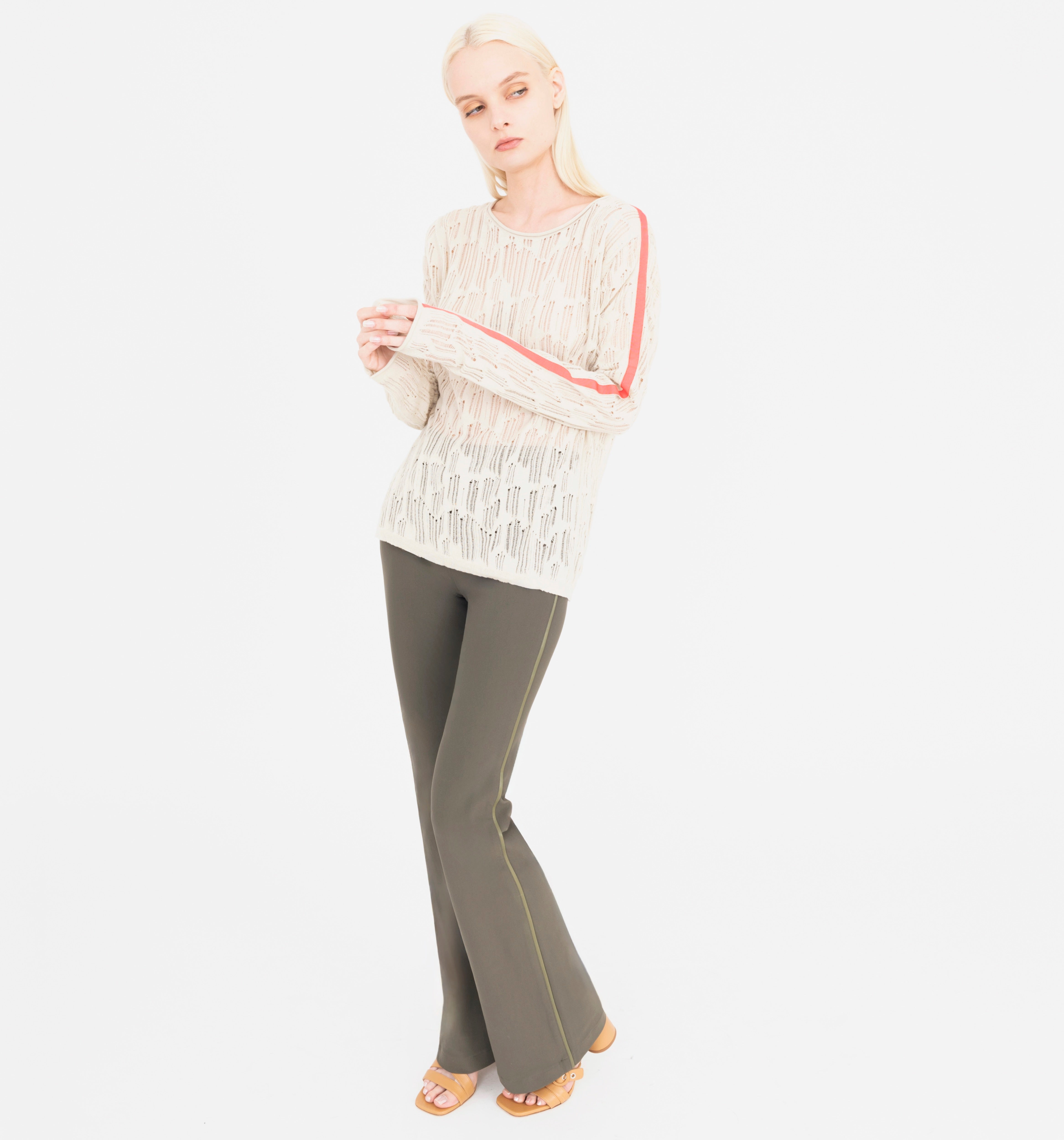 Woman wearing a beige top with orange accents and green pants on a white background