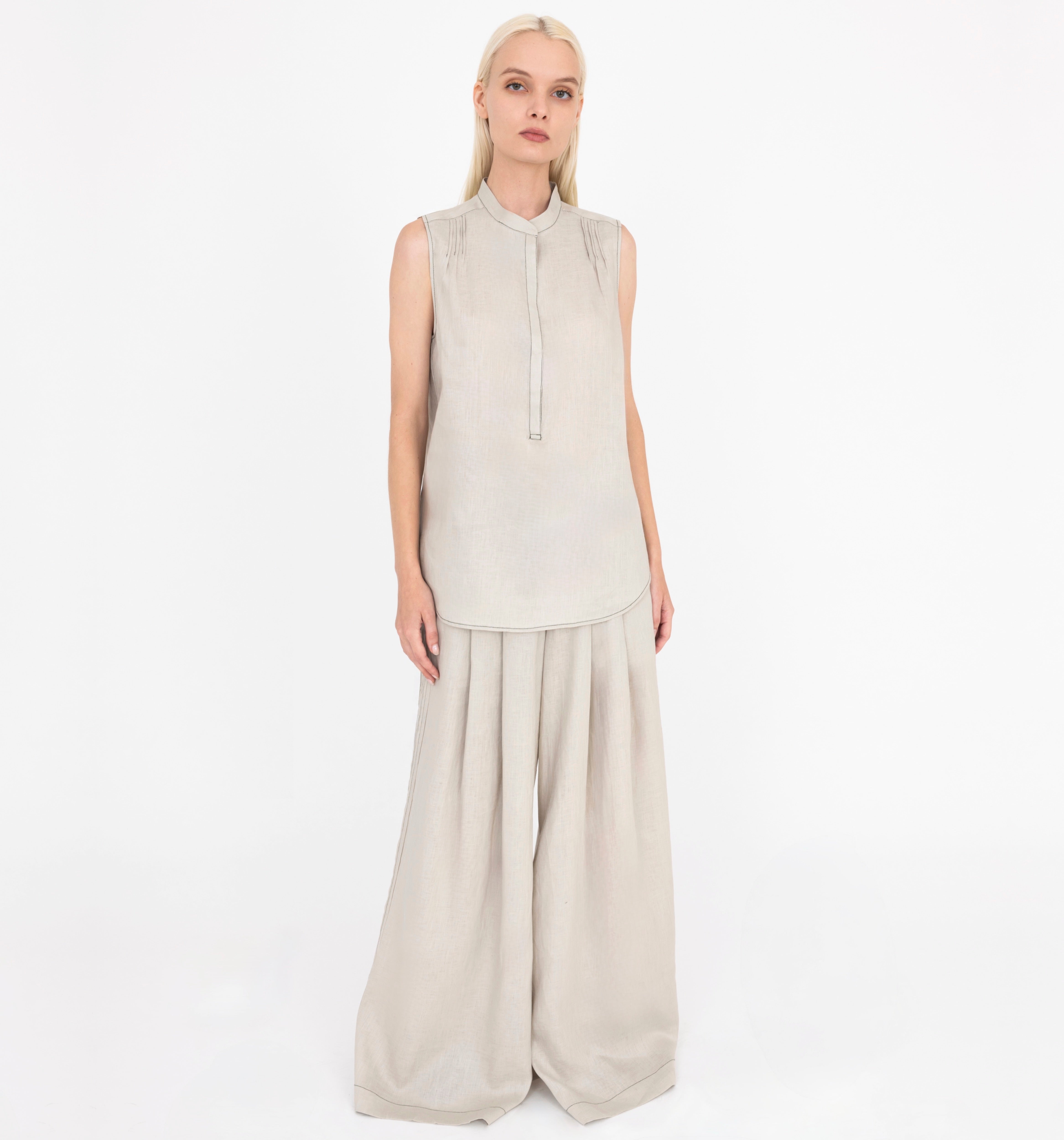 Woman wearing a beige sleeveless top and wide-leg pants on a white background