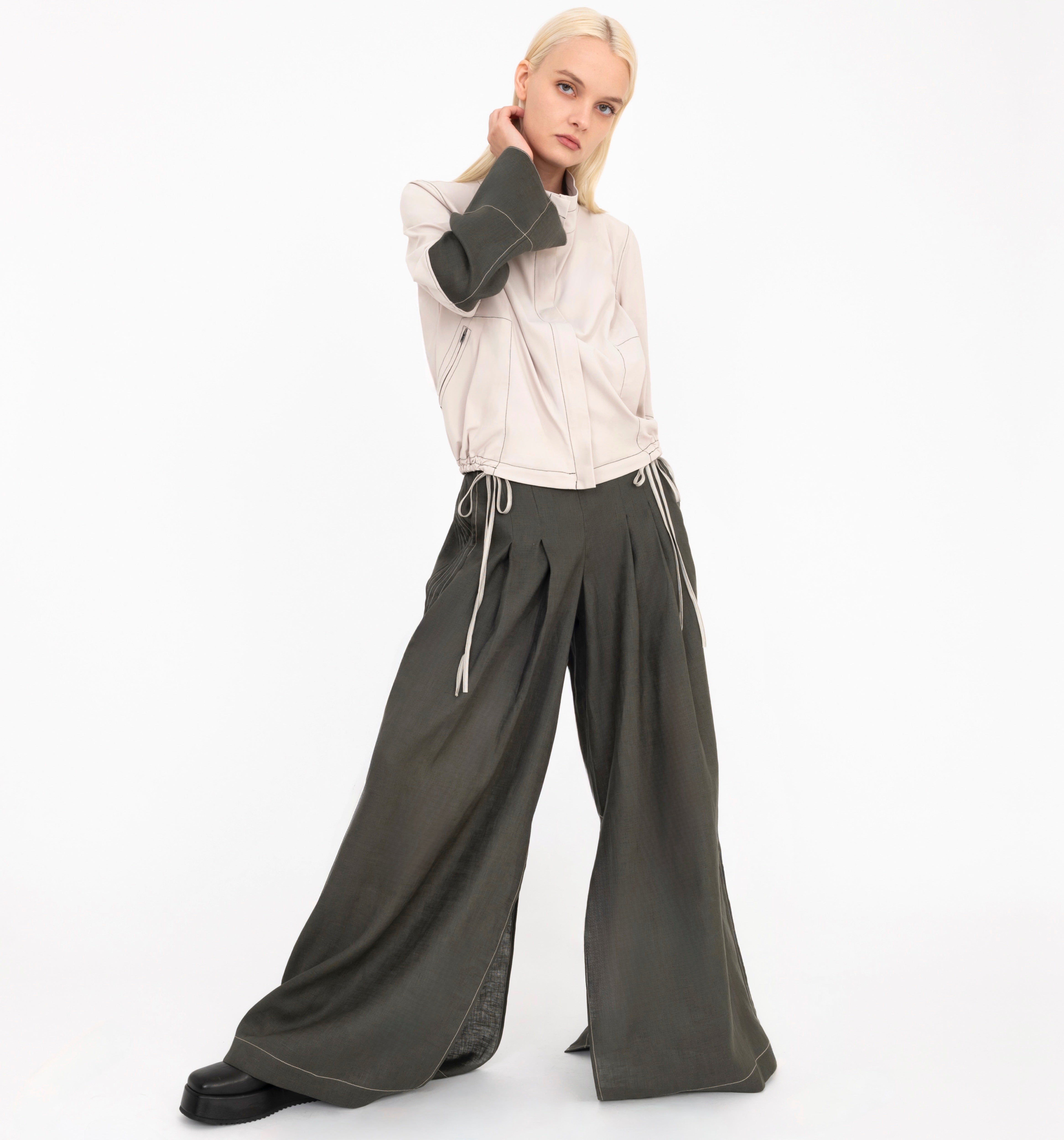 Woman wearing a beige jacket and green wide-leg pants on a white background