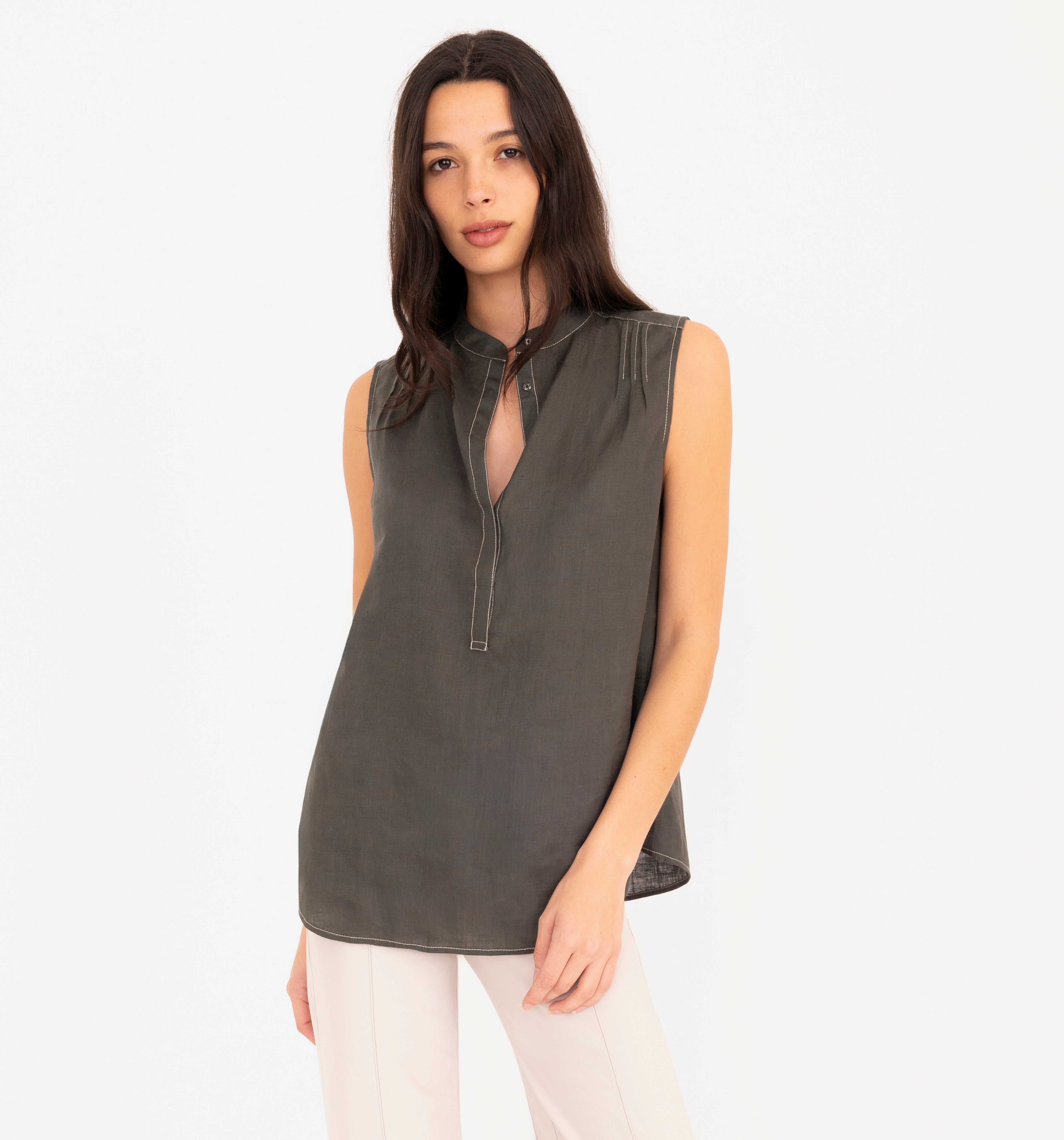 Woman wearing a sleeveless pine green top and beige pants on a white background