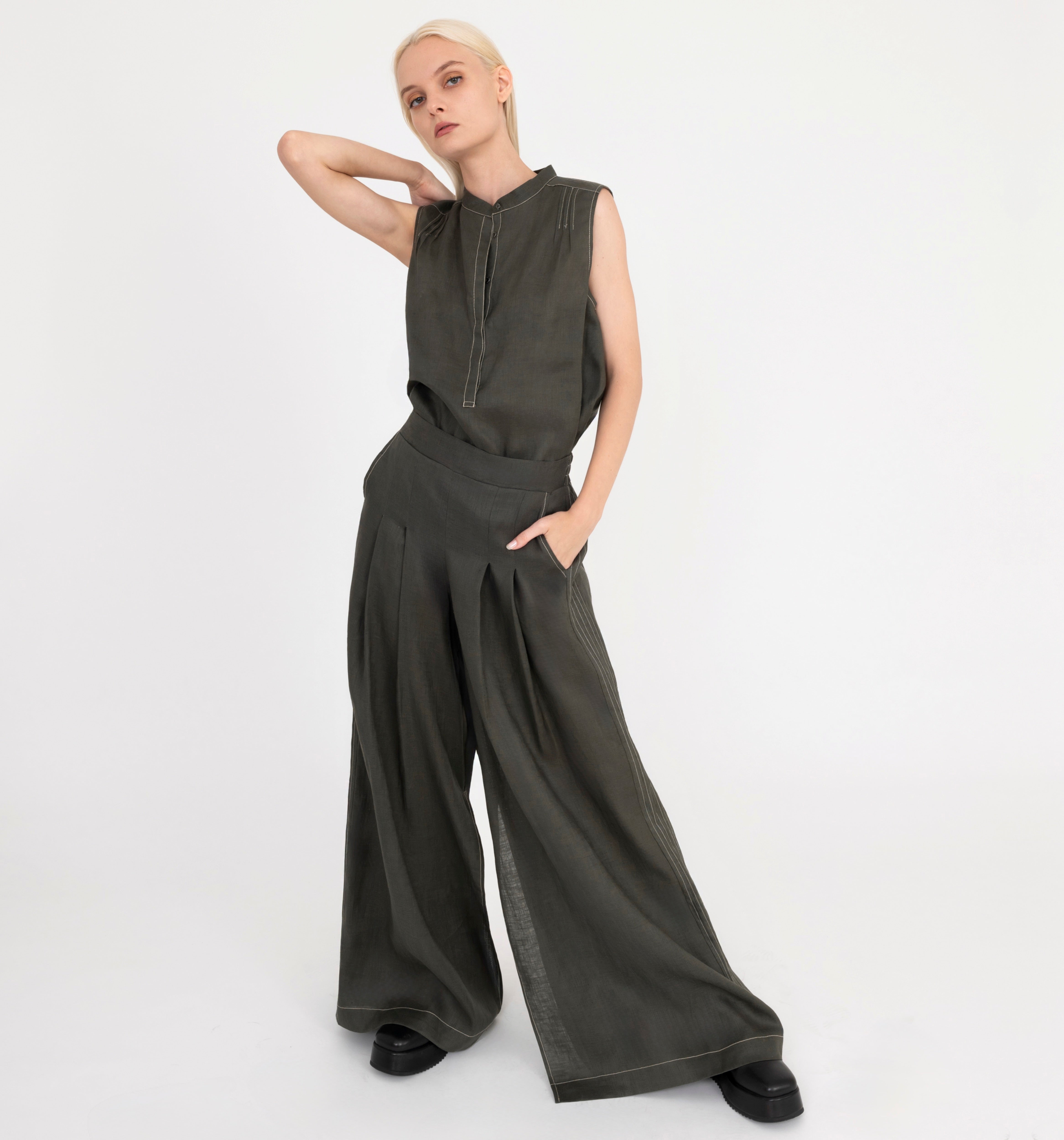 Woman wearing a sleeveless pine green top and wide-leg pants on a white background