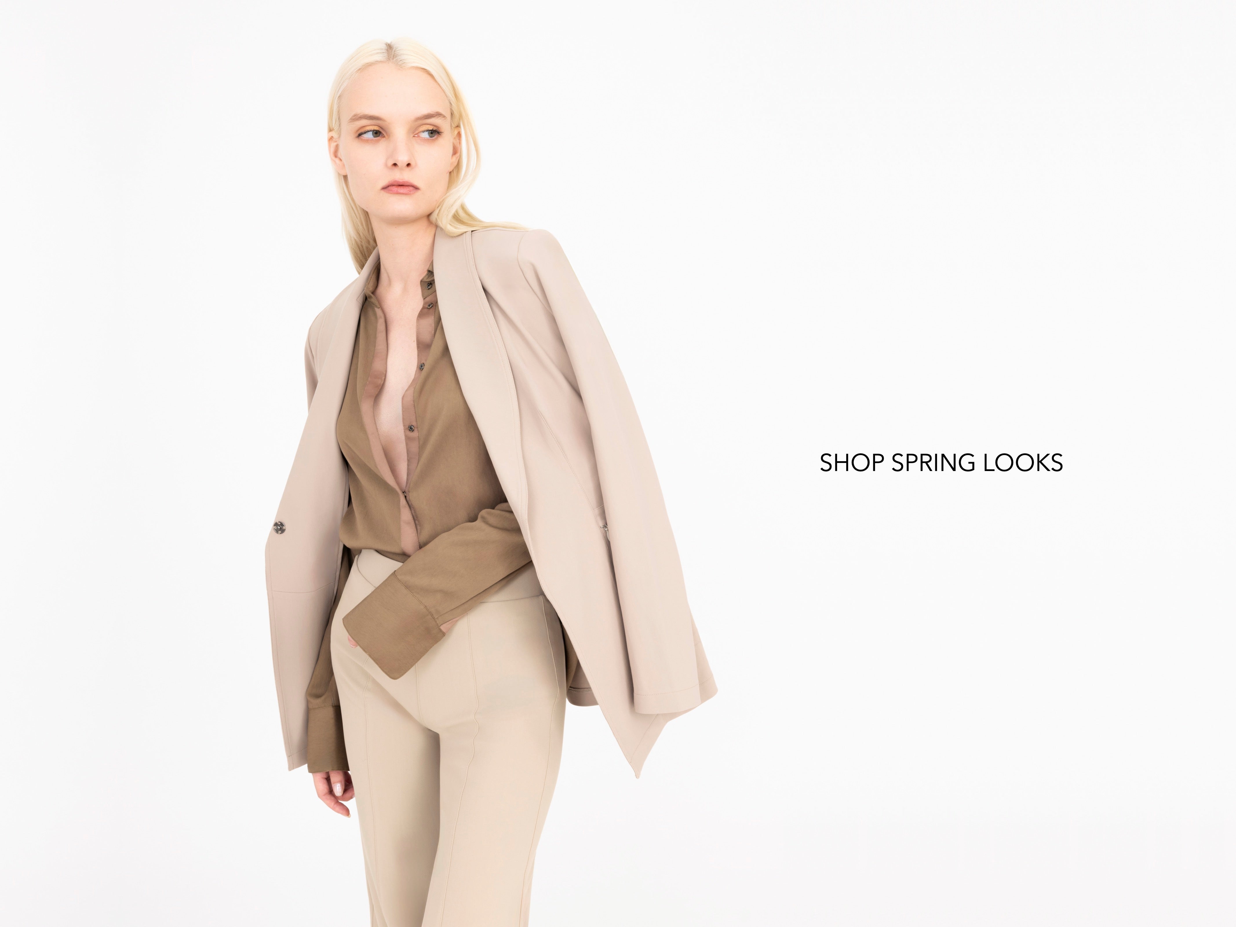 Woman wearing a beige coat over a brown shirt and beige pants on a white background with 'Shop Spring Looks' text.