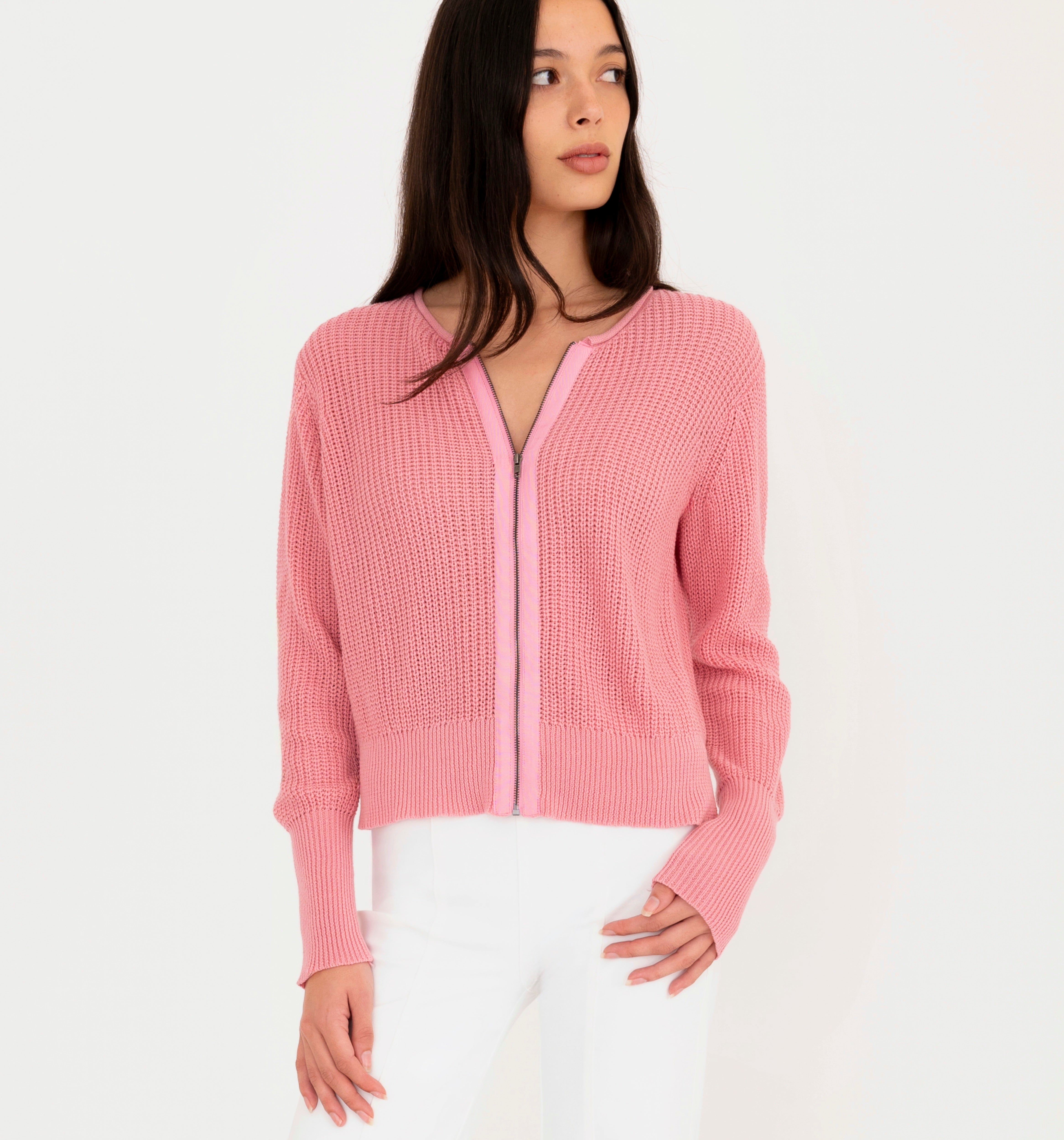 Woman wearing pink sweater and white pants on a white background
