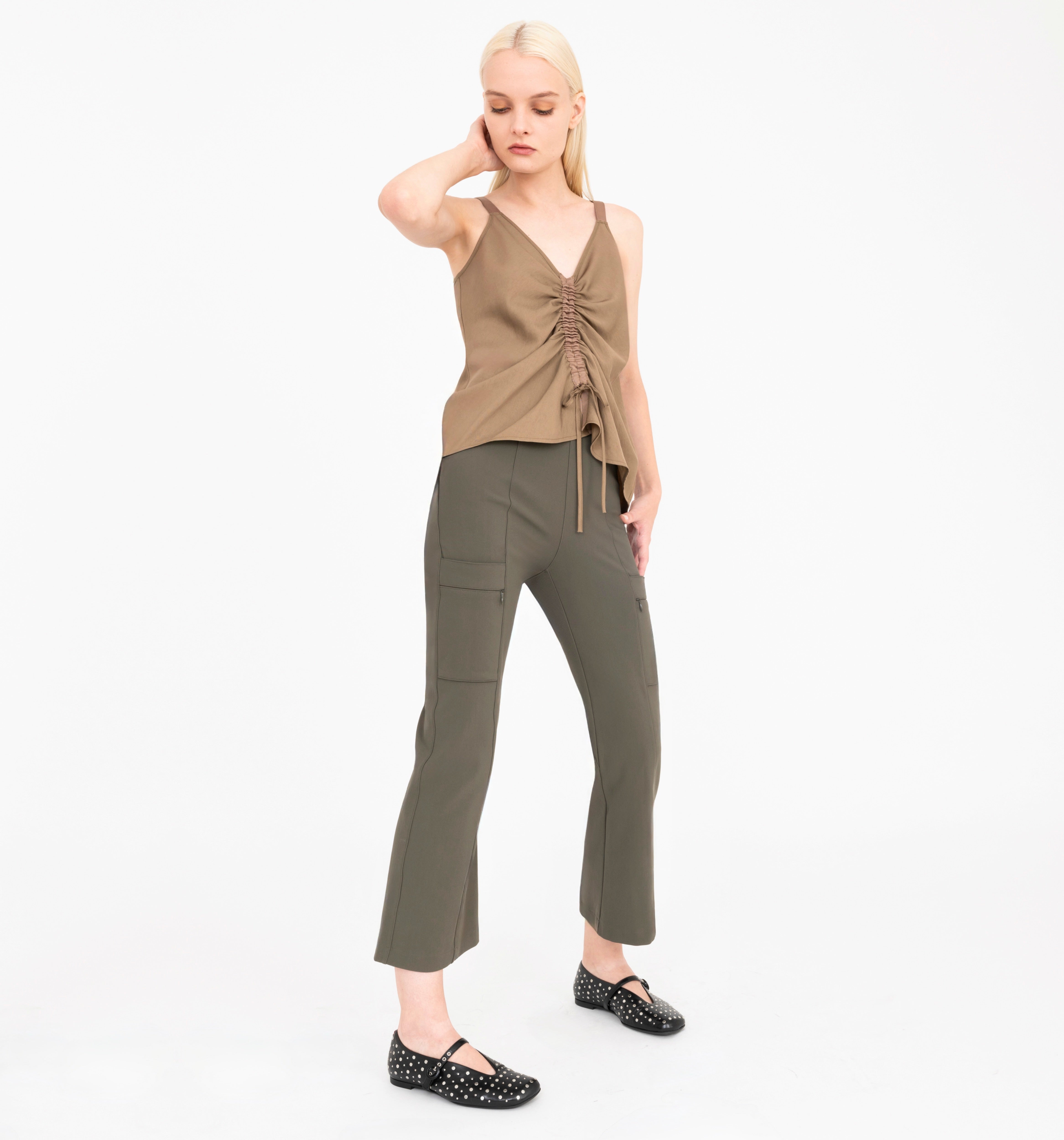 Woman wearing brown sleeveless top and green pants on a white background