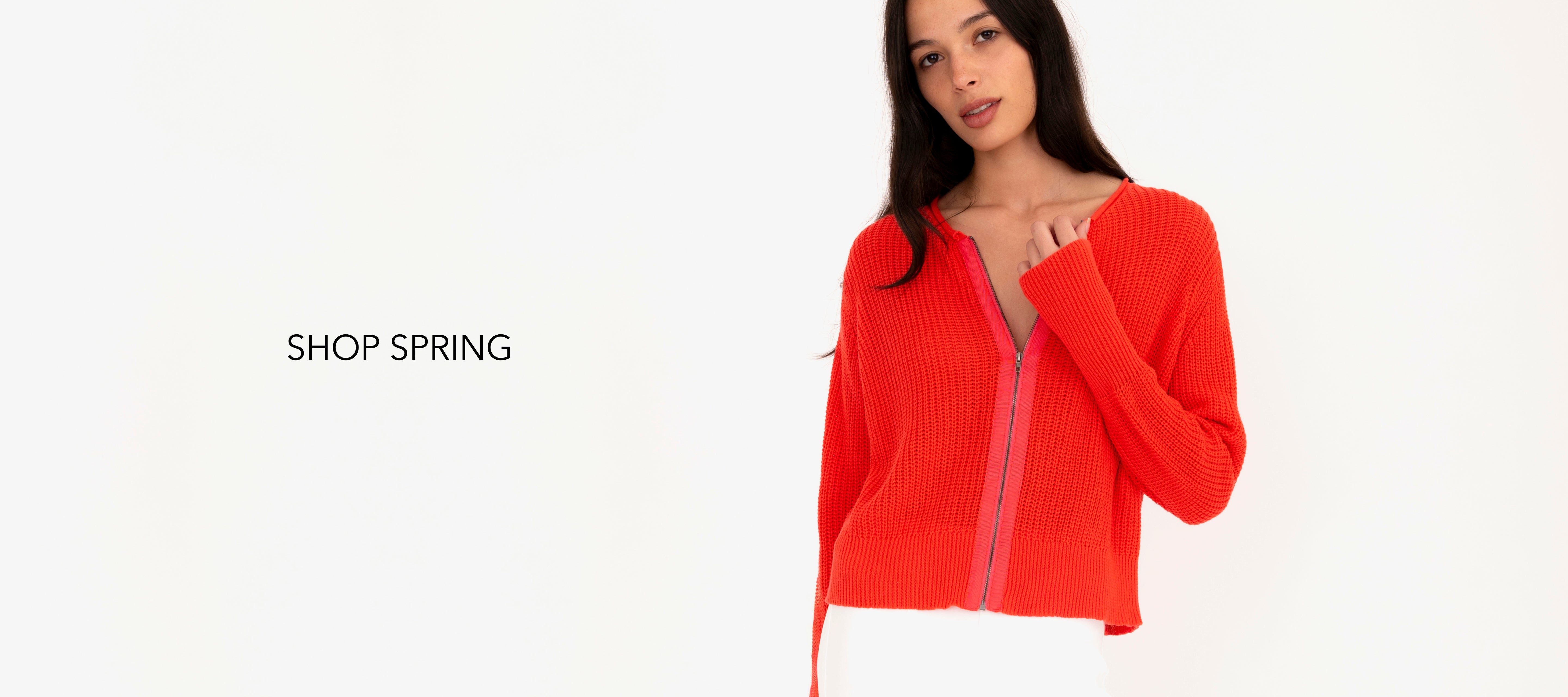 Woman wearing a orange zip-up sweater on a white background with 'Shop Spring' text.