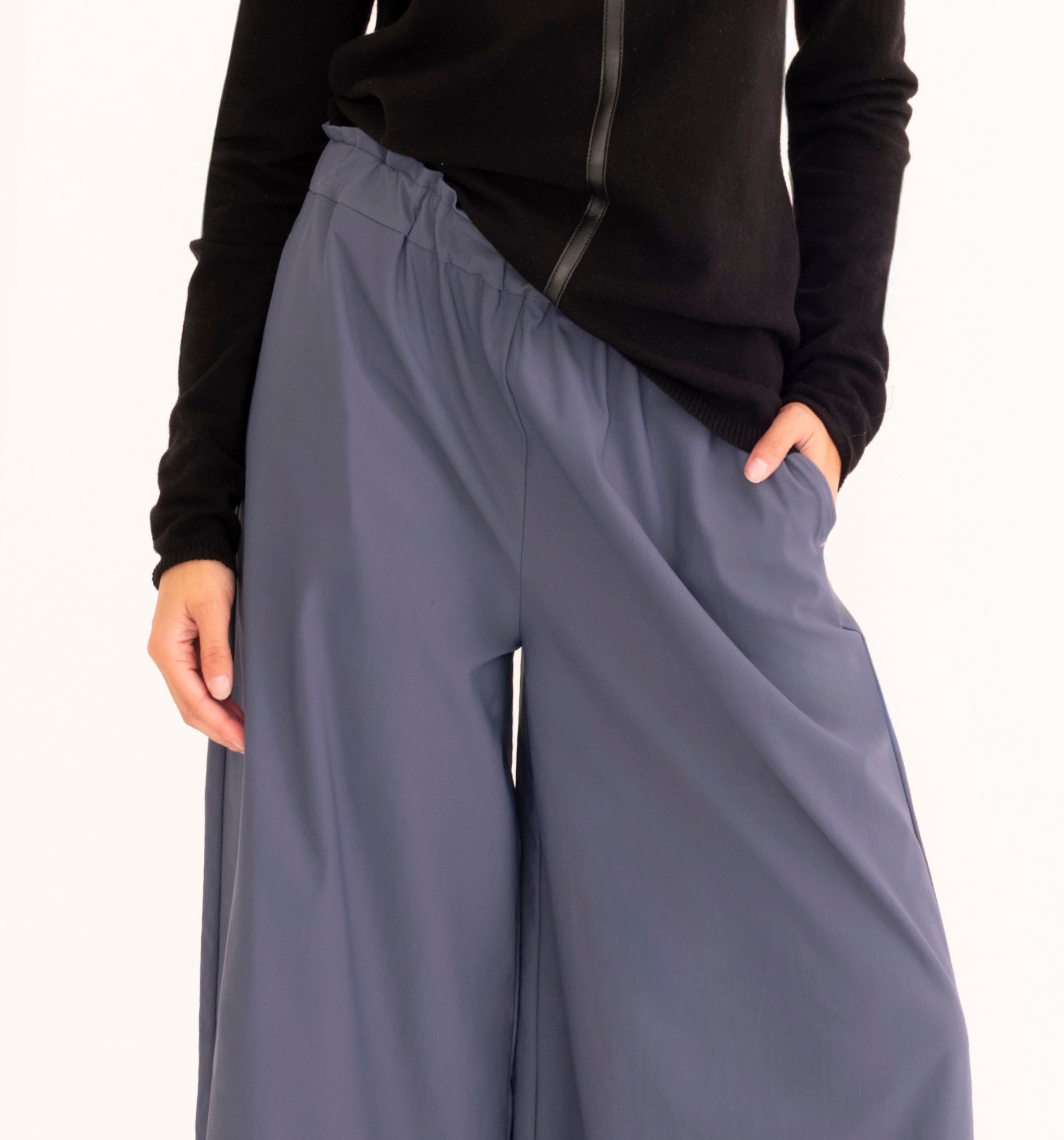 A person wearing wide-leg slate blue pants with a black long-sleeve top, shown from the chest down against a plain white background.