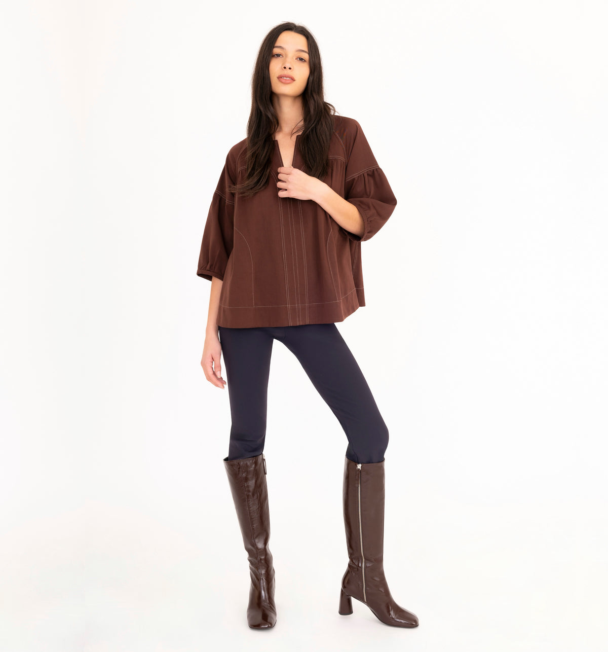 A woman modeling a brown short-sleeve denim top with contrast stitched details, paired with dark navy leggings and brown knee-high boots, against a plain white background.