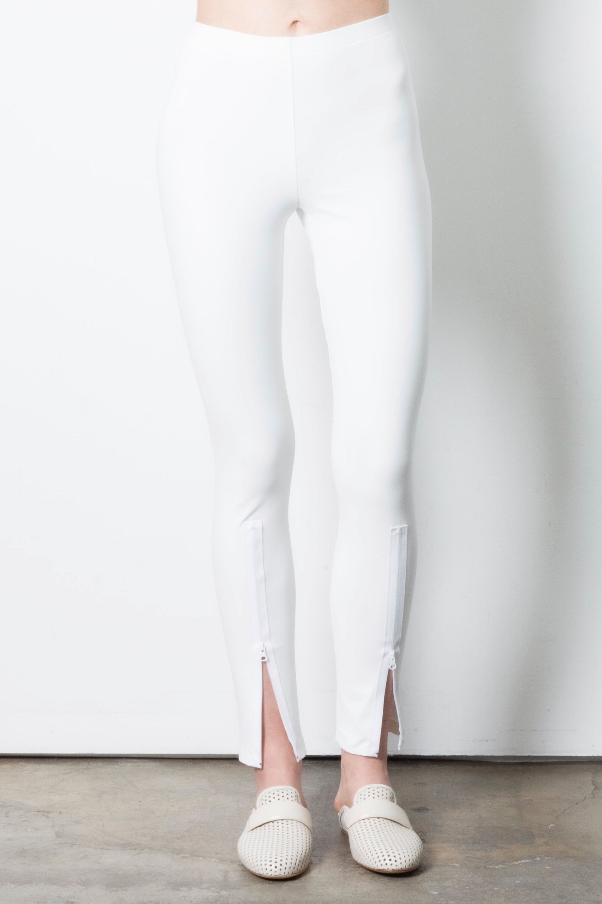 Person wearing white leggings with a slit on a plain background