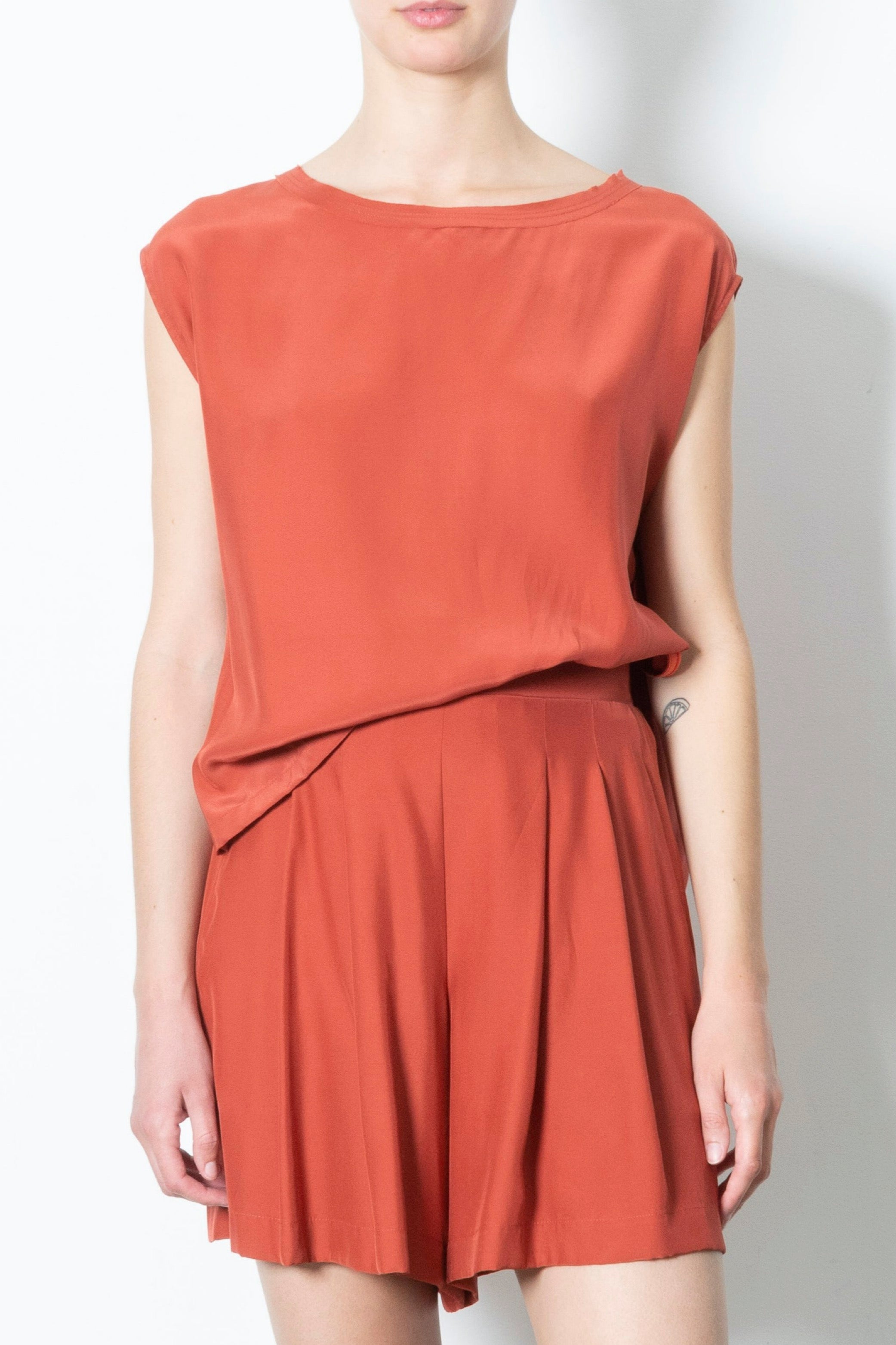 Person wearing a rust-colored sleeveless top and short set on a plain background