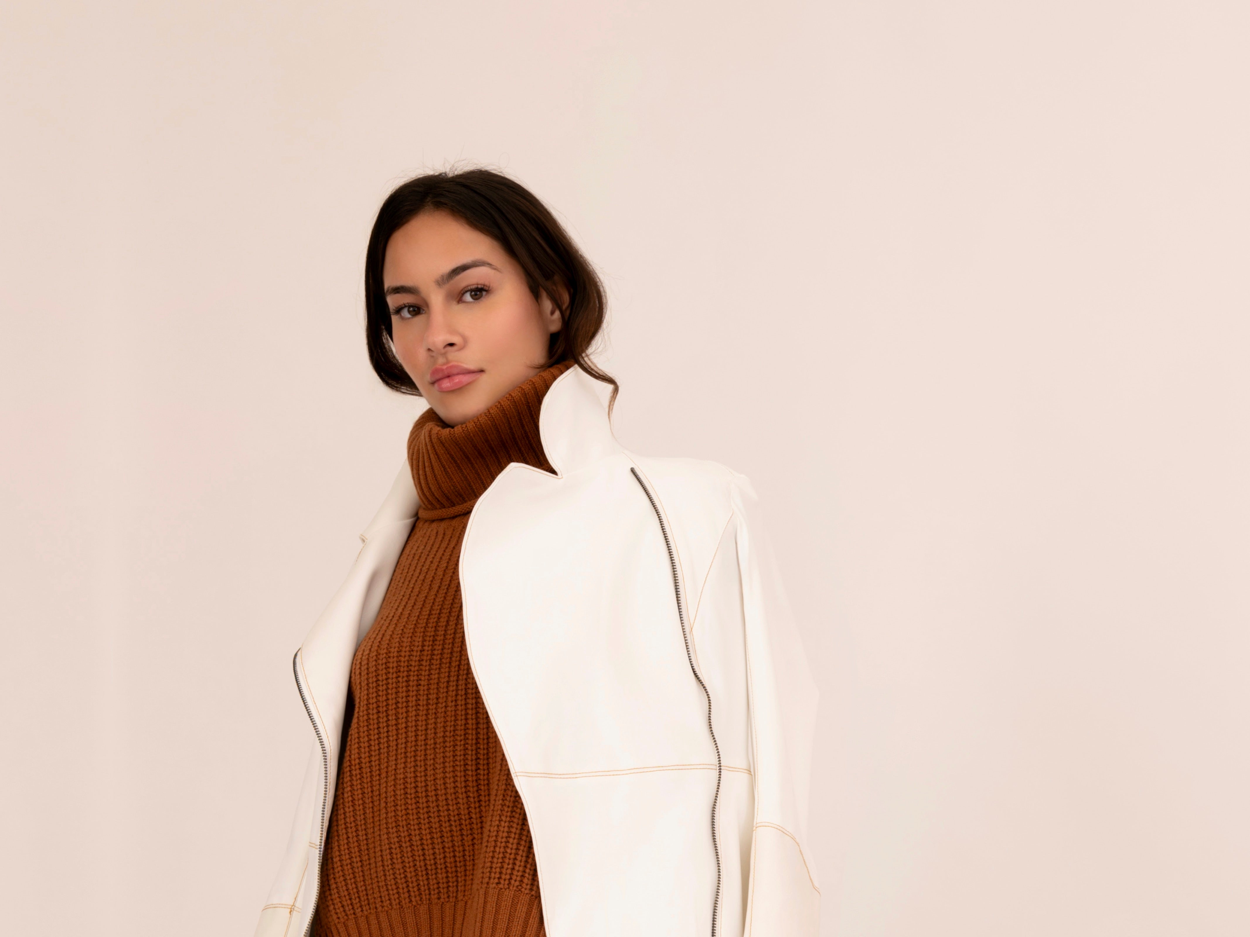 Woman wearing a white coat over a brown sweater on a plain background
