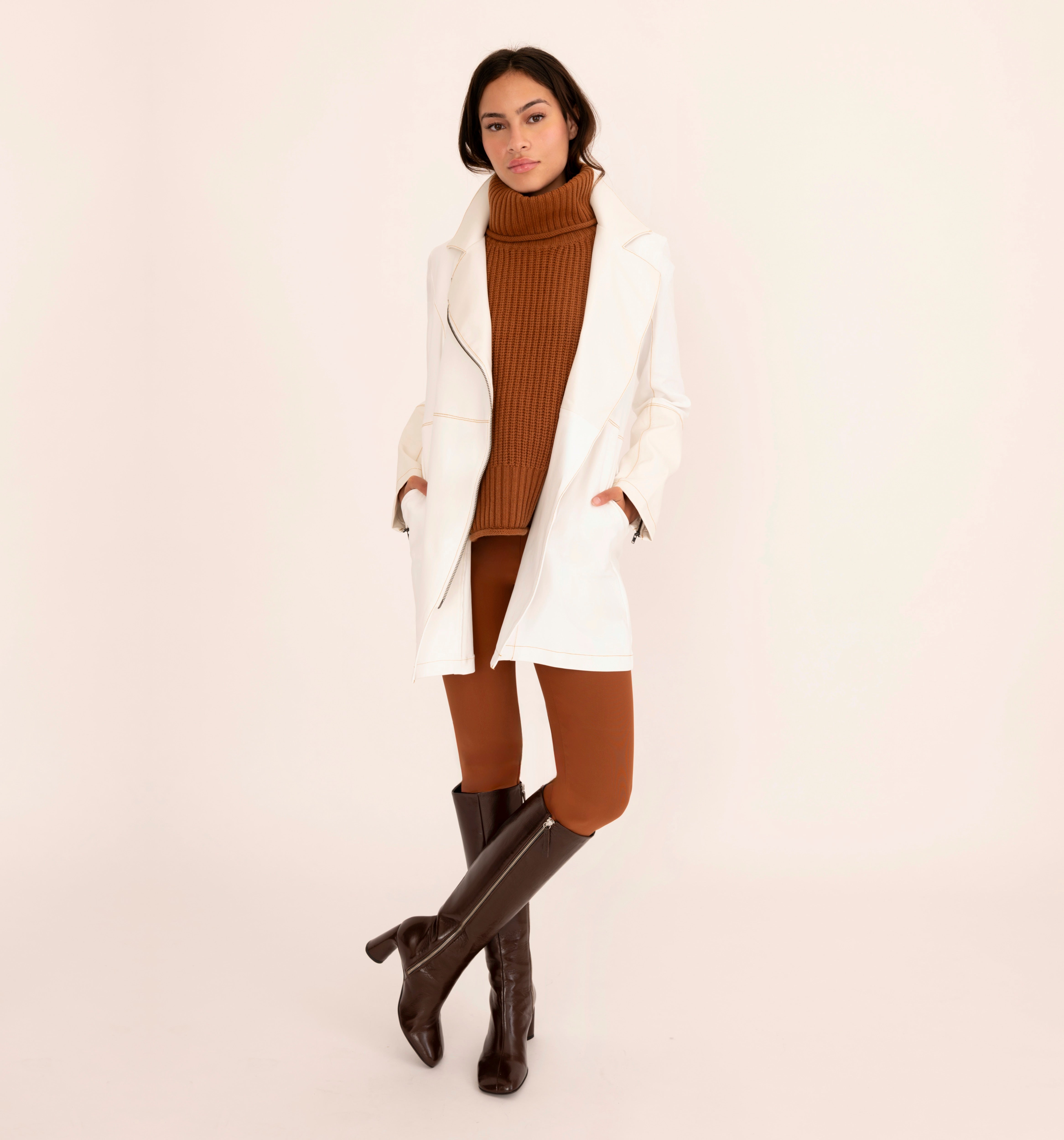 Woman wearing brown sweater and pants with a white coat on a white background