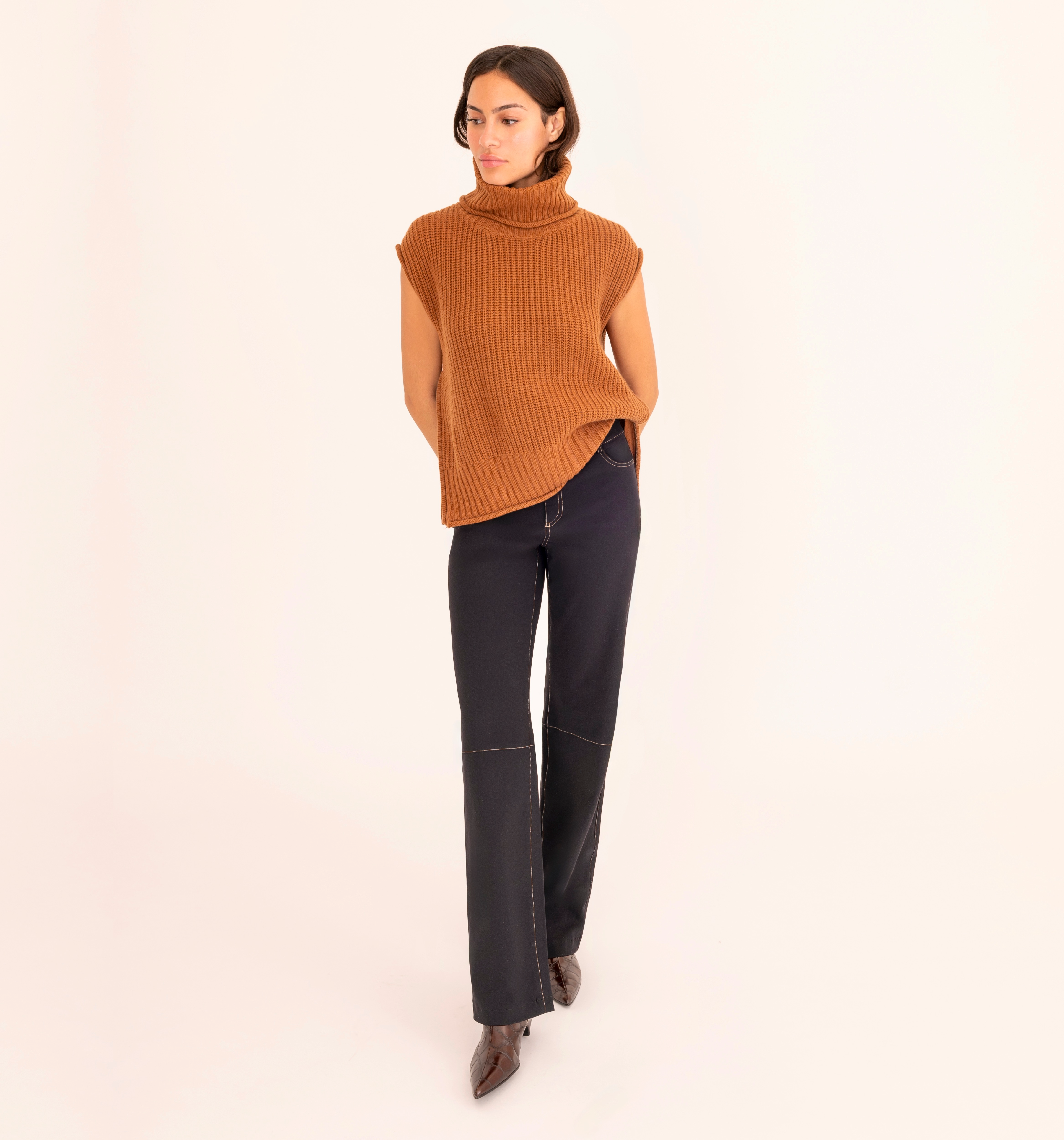 Woman wearing a brown sleeveless ribbed sweater and black pants on a beige background