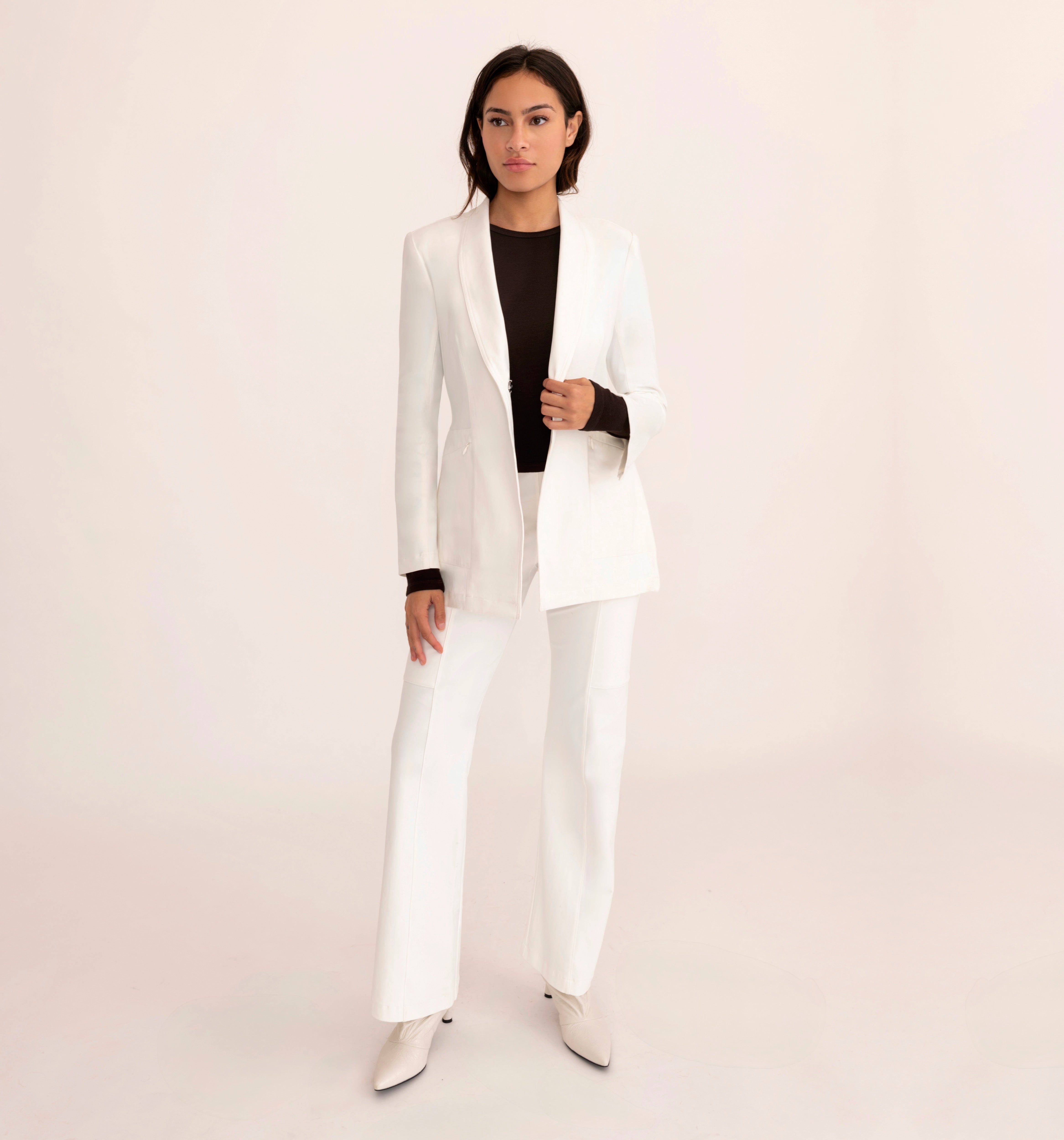 Woman wearing a white suit with a brown top on a light pink background