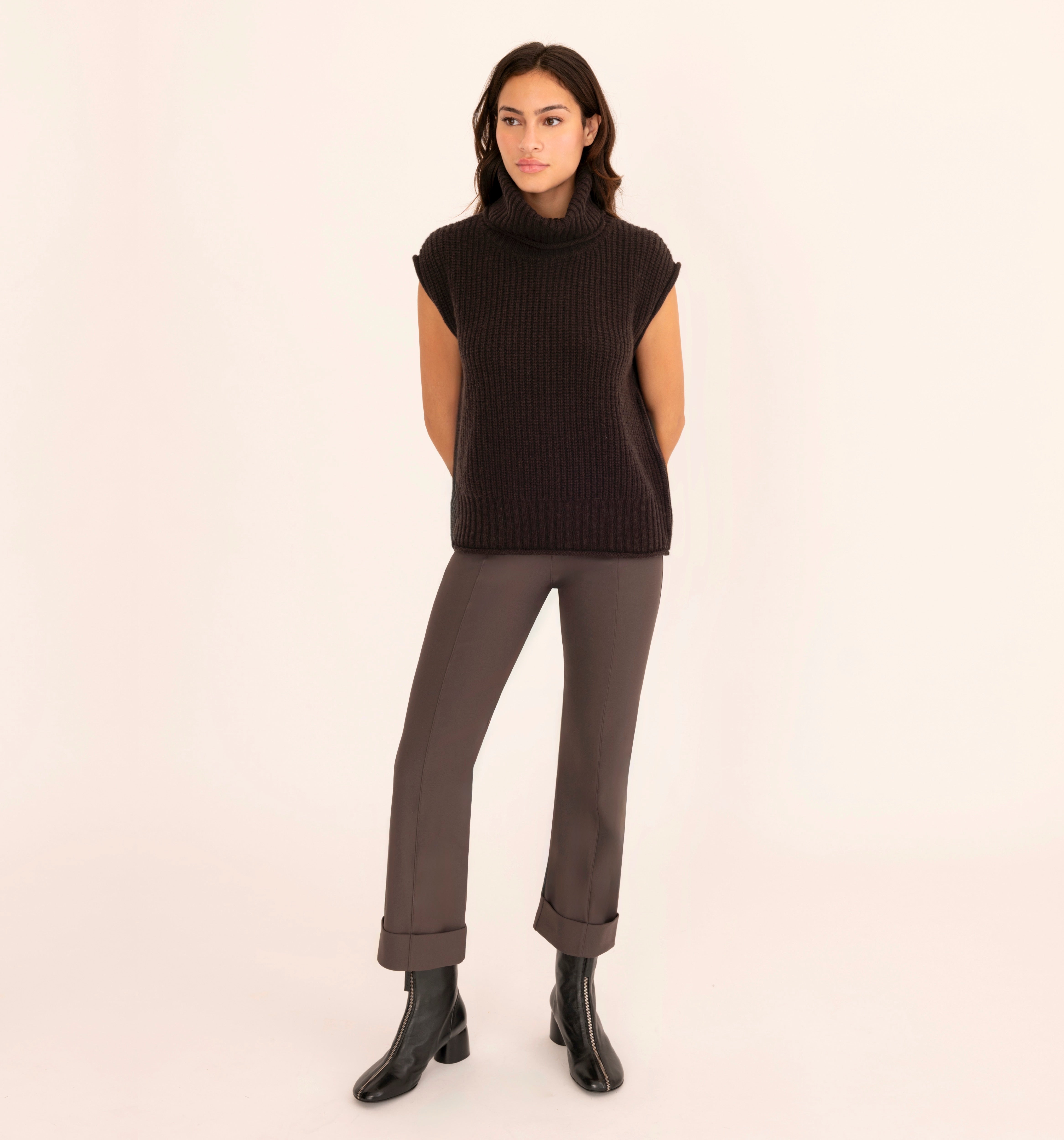 Woman wearing a brown sleeveless sweater and pants on a beige background