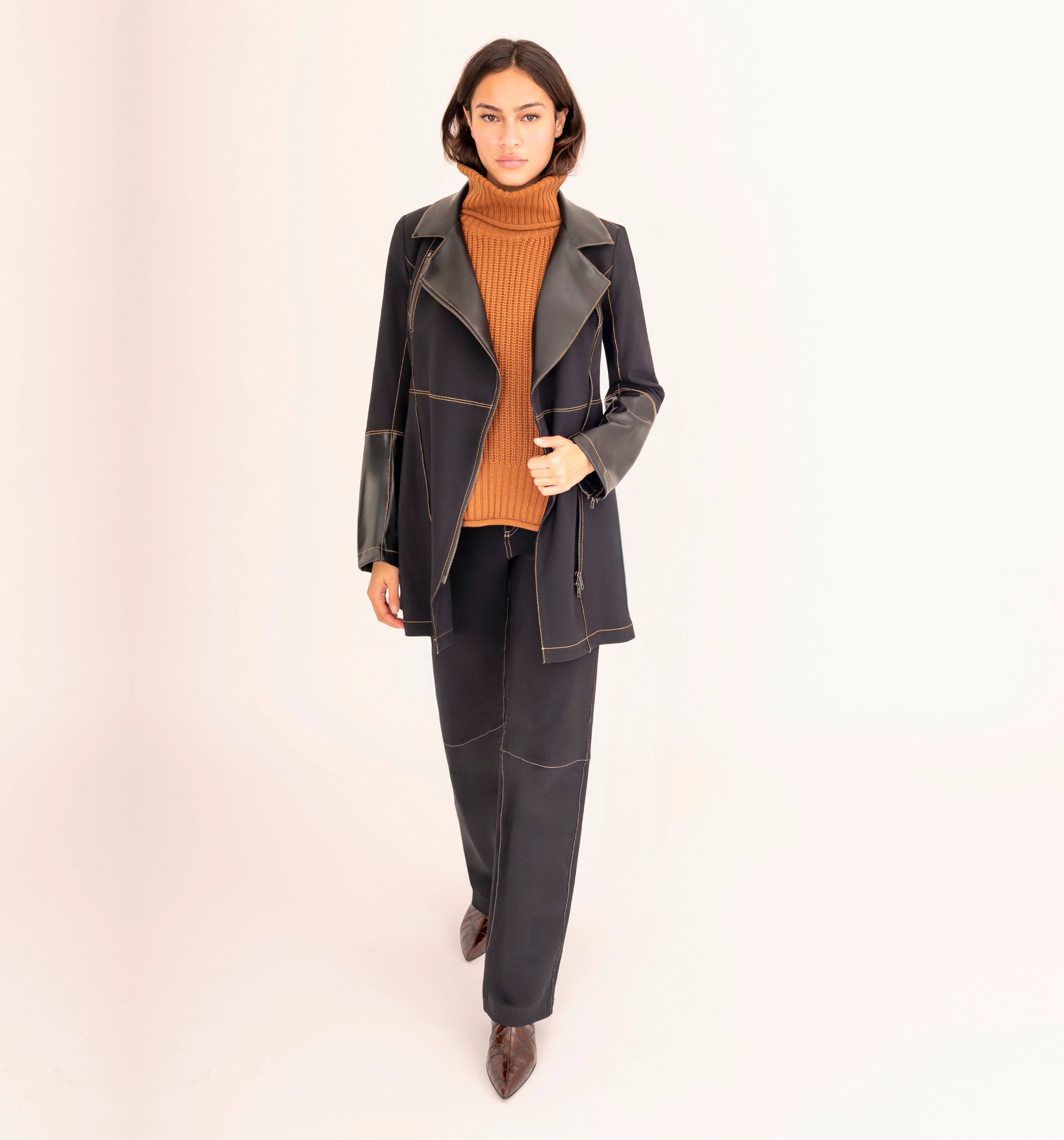 Woman wearing a black coat and pants with a mustard sweater on a beige background